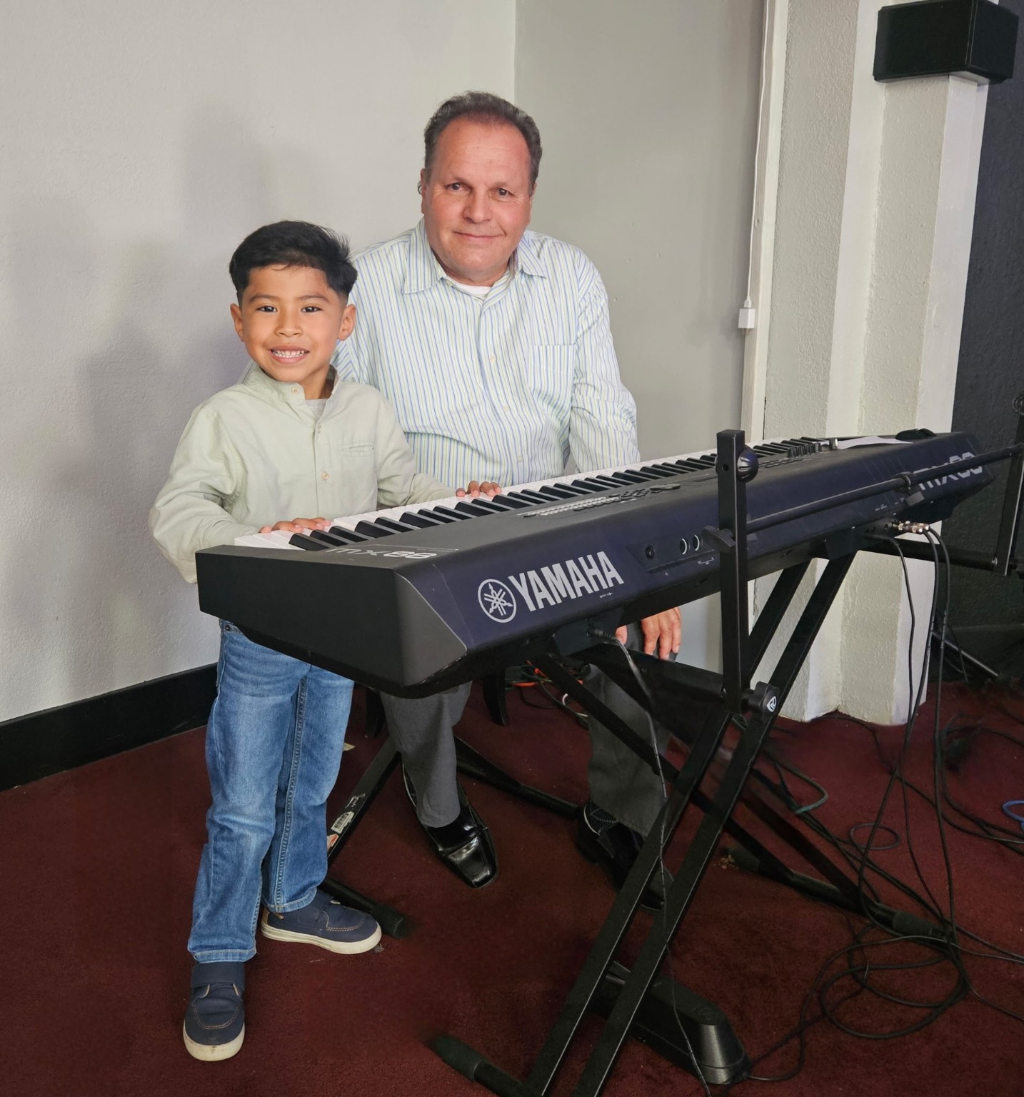 A young boy at the keyboard beside a musician of the church